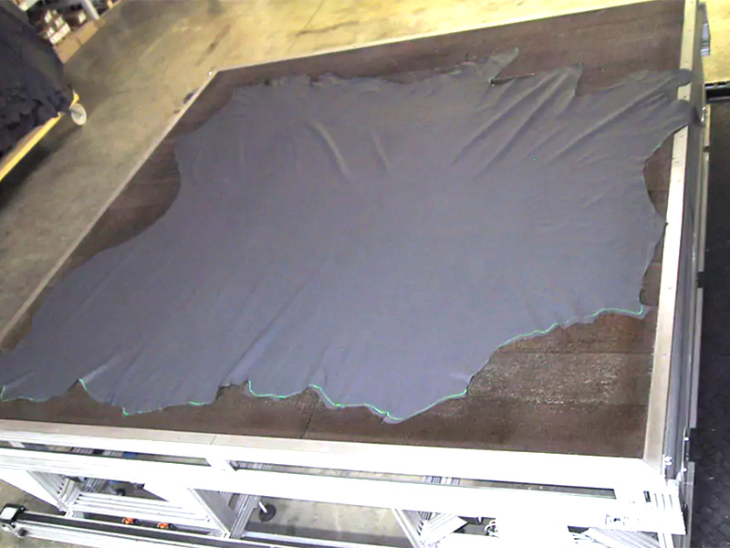 Lederhaut auf einem Arbeitstisch ausgebreitet – grüne SL-Laser Linien markieren präzise Schnittkonturen für die Weiterverarbeitung.