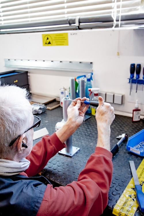 Employee at a workbench assembling precision components with a hand tool in production.