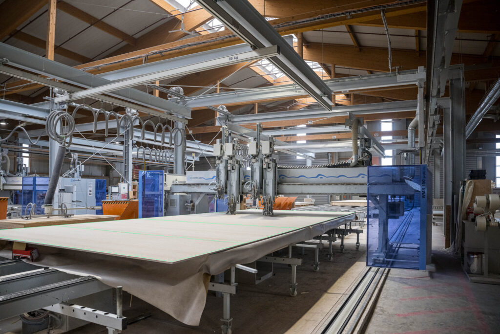 Moderne Fertigungsanlage für Holzfertigteile – CNC-Maschine bearbeitet große Platten, grüne SL-Laser Linien markieren präzise Schnitt- und Positionierpunkte.