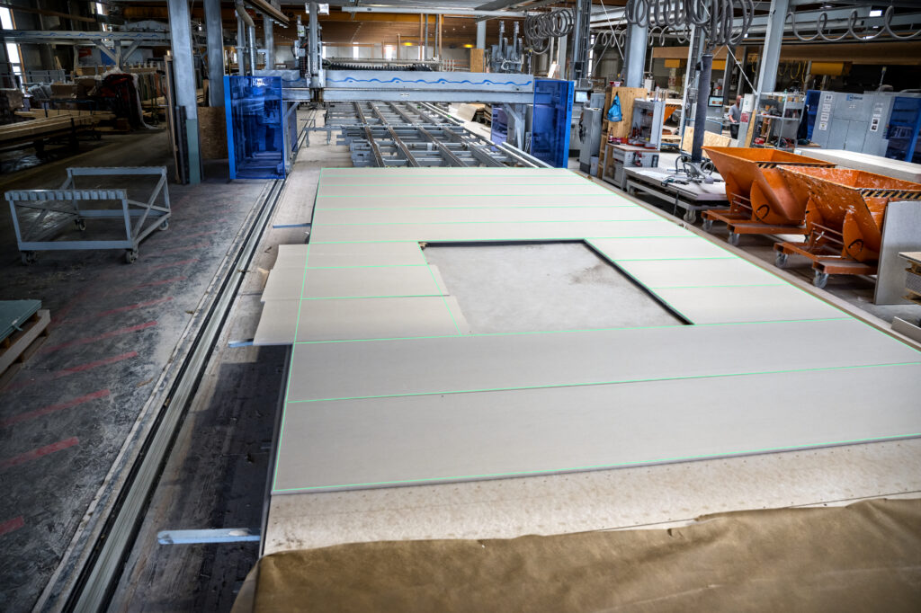 Produktionsanlage für Holzfertigteile – grüne SL-Laser Linien markieren exakte Schnitt- und Aussparungsbereiche auf großen Platten.