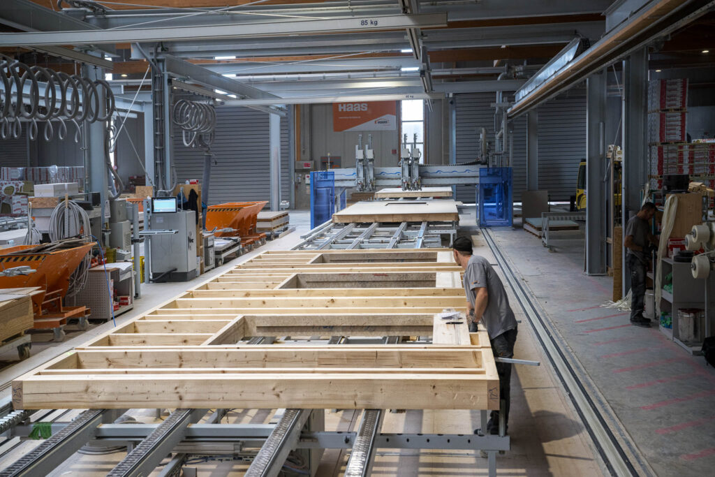 Fertigungshalle für Holzbau – Mitarbeiter arbeitet an großen Holzrahmenelementen, unterstützt durch präzise Laserprojektionen von SL-Laser.