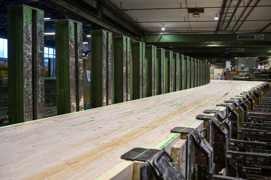 Produktionshalle mit einer langen Holzbearbeitungsanlage – grüne Laserlinien von SL-Laser markieren präzise Schnitt- und Positionierpunkte auf den Holzplatten.