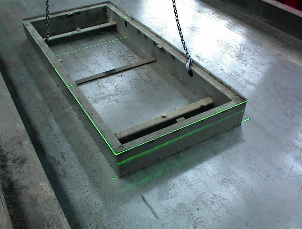 Steel formwork is precisely aligned on a concrete production mold using green laser lines.