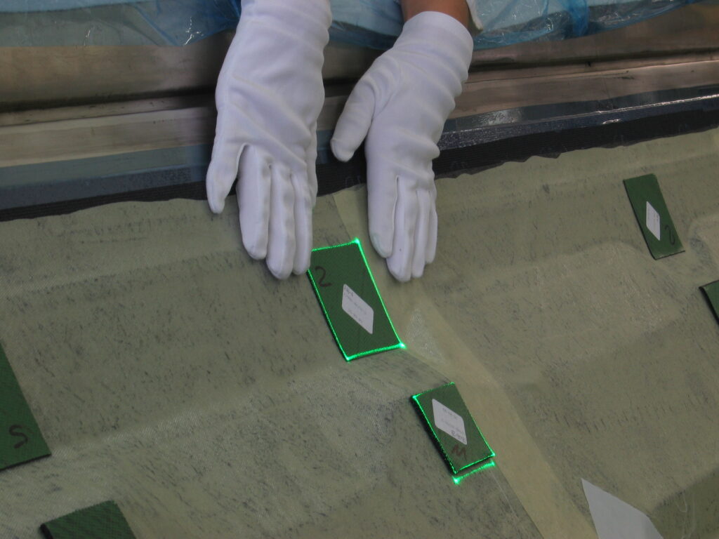Un ouvrier portant des gants blancs positionne des marqueurs verts sur un composant composite – la projection laser SL montre les points de placement exacts.