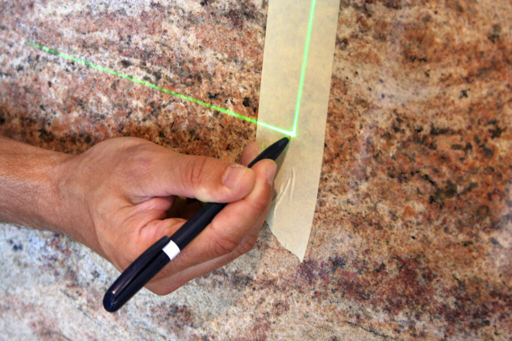 Hand marks a line on stone with a pen along a projected green laser line from SL-Laser.