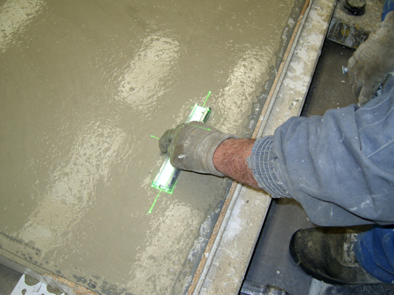 Worker smoothes fresh concrete with a template that is precisely positioned by green laser lines.