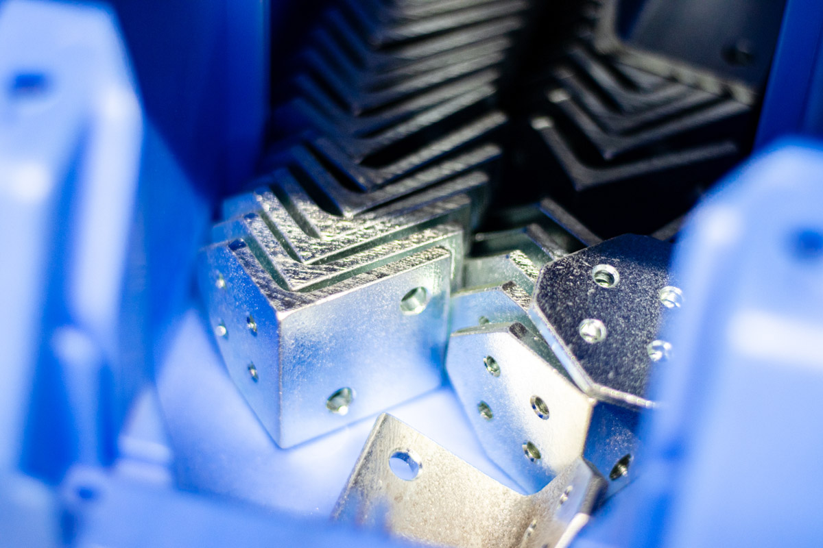 Nahaufnahme von glänzenden Metallbauteilen mit Bohrungen, gestapelt in einer blauen Vorrichtung.