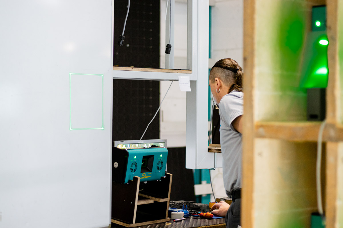 Employee checks an SL laser device in a test environment while a green laser rectangle is projected onto a white projection surface.