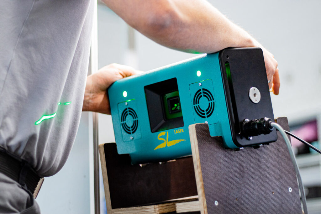 Un employé aligne un dispositif laser vert SL sur un support qui projette des lignes laser sur une surface.