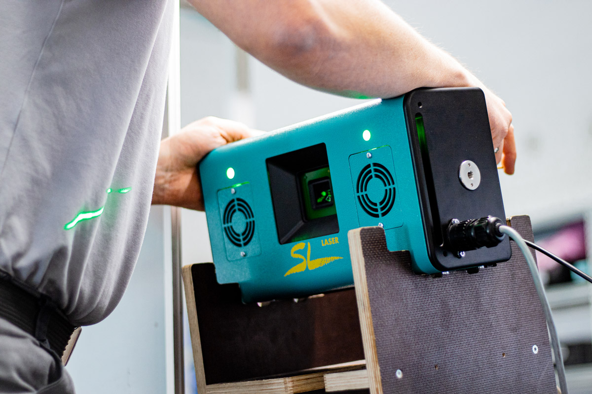 Employee aligns a green SL laser device on a mount that projects laser lines onto a surface.