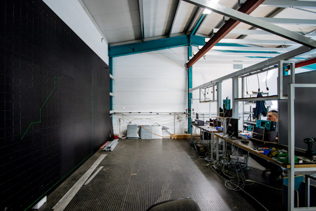 Testlabor mit großflächiger schwarzer Projektionswand, auf der grüne Laserlinien sichtbar sind, daneben mehrere SL-Lasergeräte an den Arbeitsplätzen.