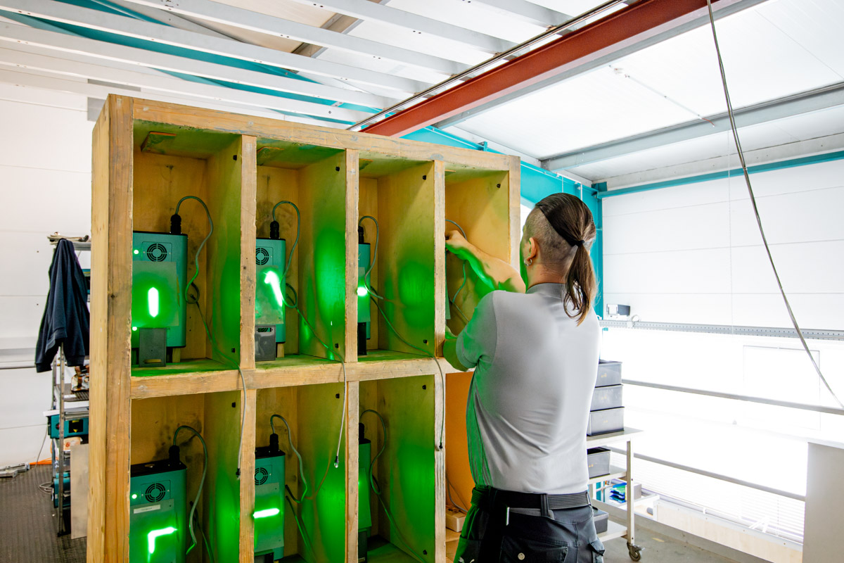 Mitarbeiter überprüft mehrere SL-Lasergeräte, die in einer Holzkonstruktion mit grünen Laserprojektionen für Test- und Kalibrierzwecke eingebaut sind.