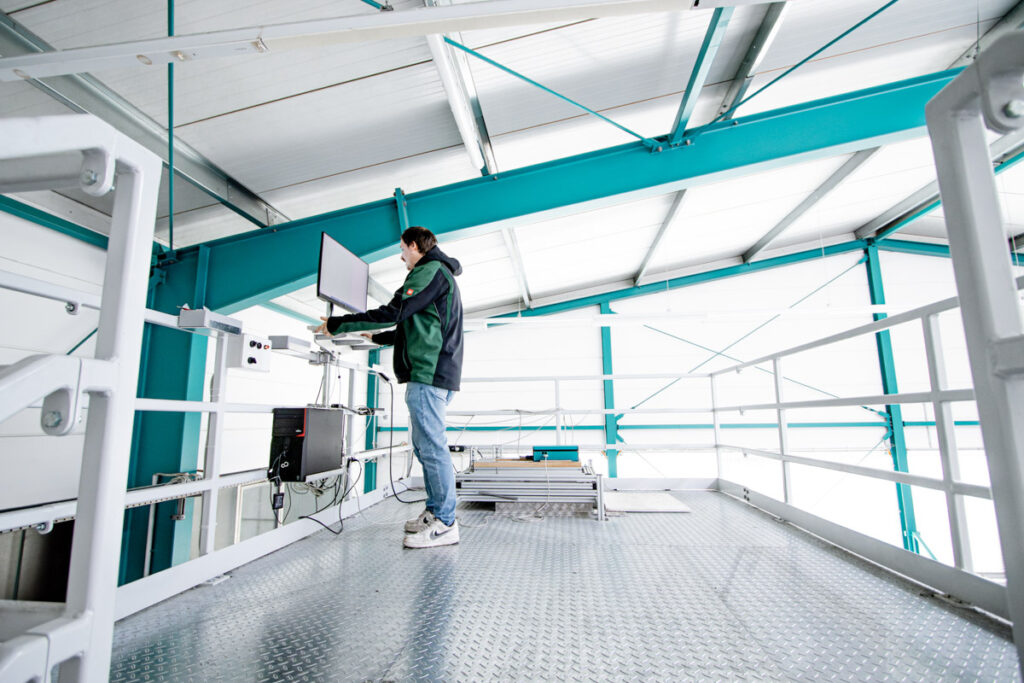 Mitarbeiter bedient Steuerungs- und Computersystem auf einer erhöhten Plattform mit Metallboden in der SL-Laser Produktion.