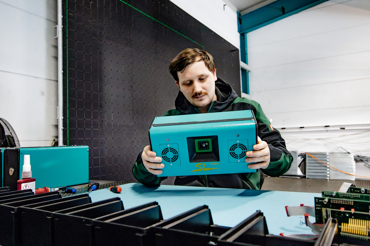 Employee in SL laser workshop checks a green SL laser device on a work table in a modern production environment.