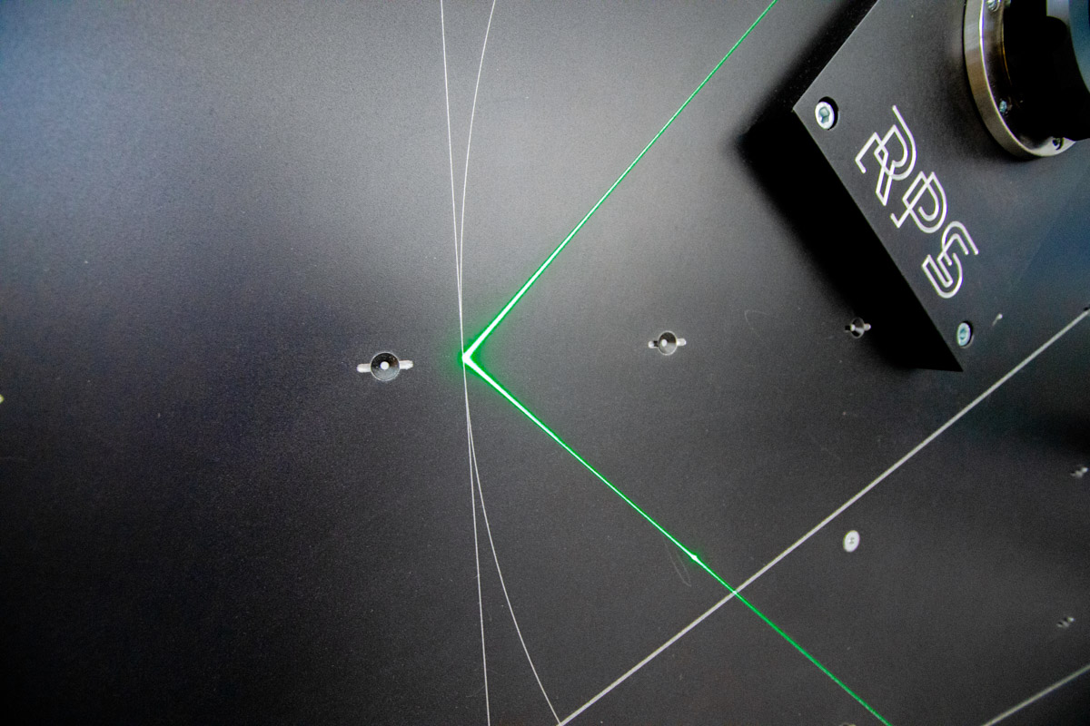 Detailaufnahme einer schwarzen Projektionswand mit grünen Laserlinien und einem montierten Referenzpunkt-System (RPS) zur präzisen Kalibrierung.