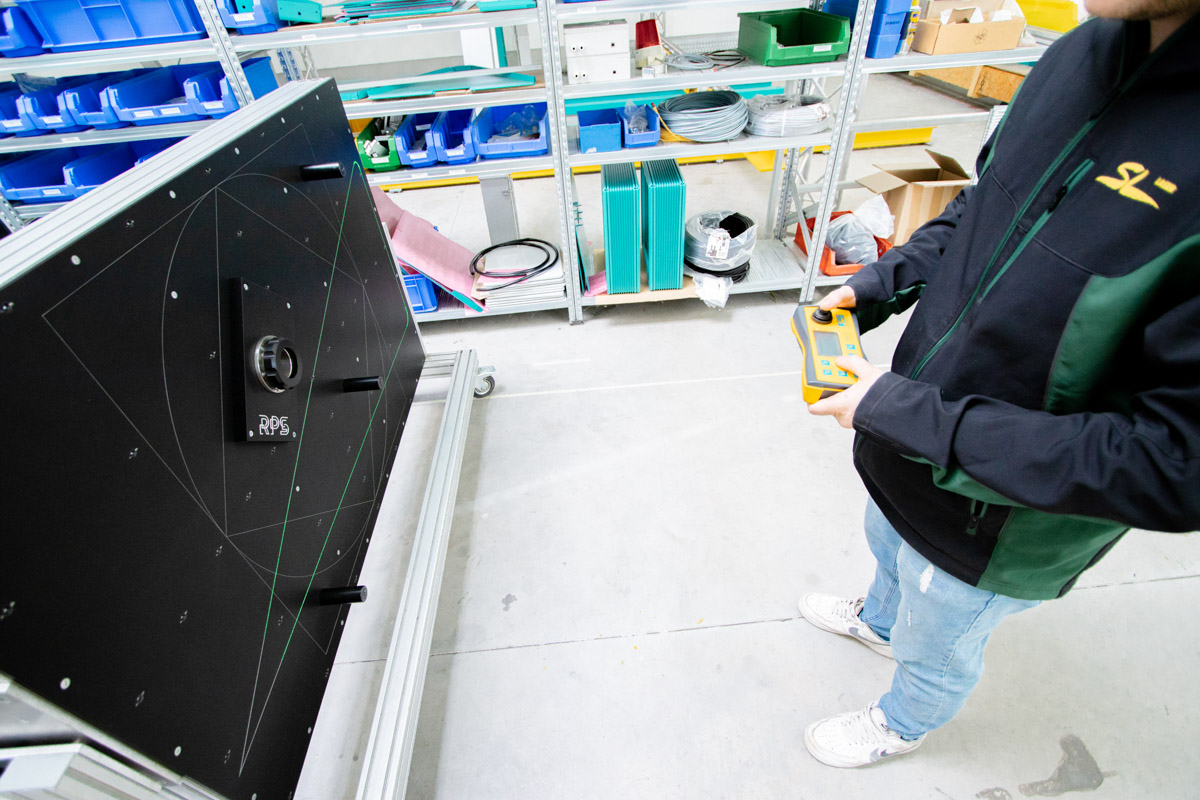 Mitarbeiter bedient mit einem Handgerät eine Kalibrierwand mit grünen Laserprojektionen und Referenzpunktsystem (RPS) in einer Werkstattumgebung.