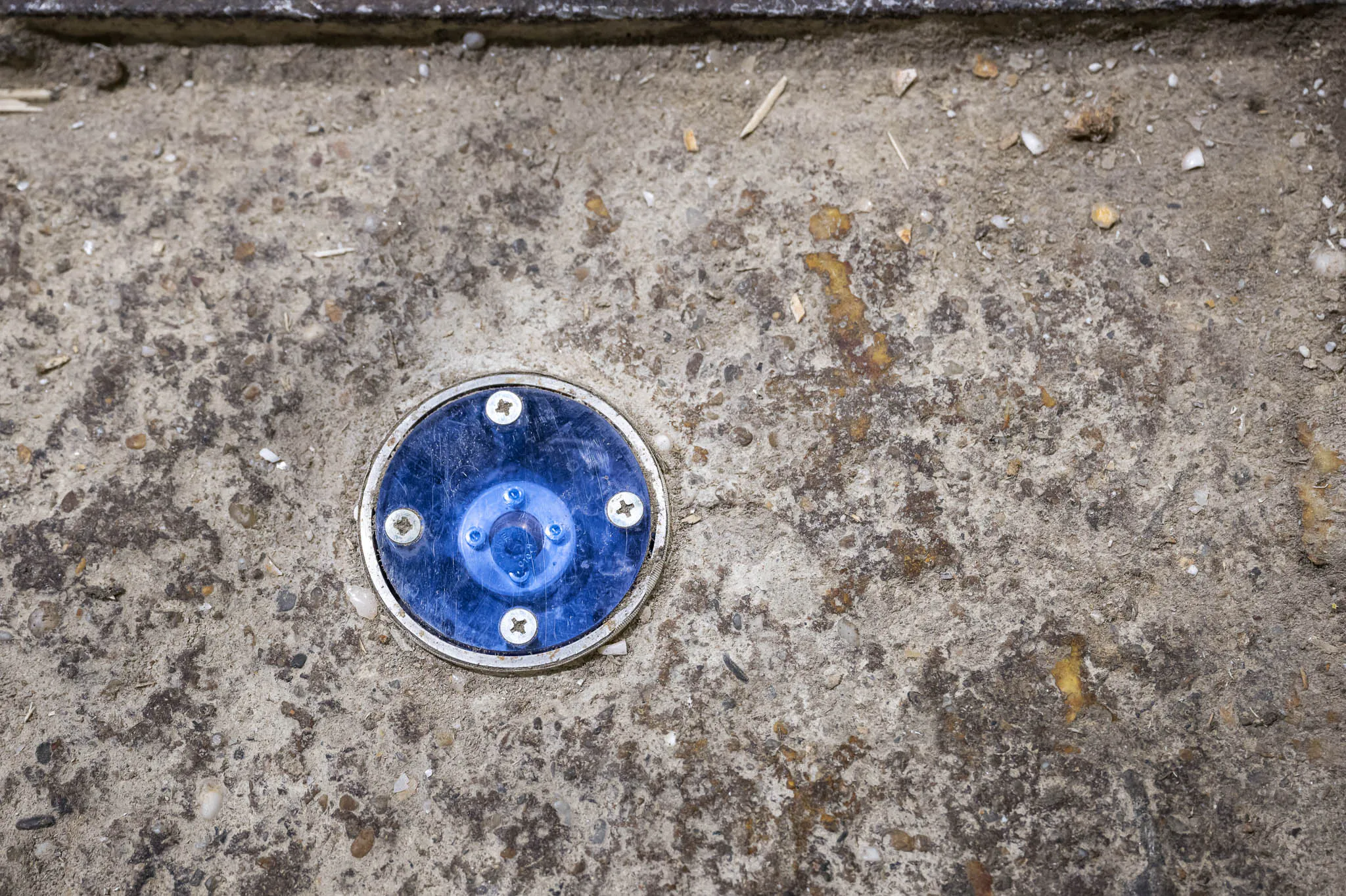 Blauer Reflektor im Hallenboden, fixiert mit Schrauben, dient als Referenzpunkt für die exakte Kalibrierung und Ausrichtung von SL-Lasersystemen.