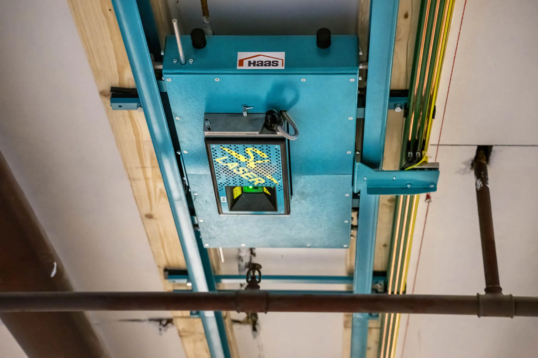 SL-Lasergerät an einer Deckenkonstruktion montiert, integriert in ein Schienensystem zur präzisen Positionierung und Projektion im industriellen Einsatz.